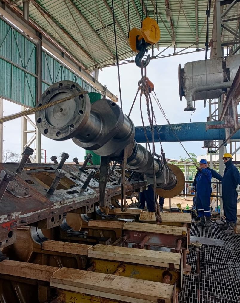 Cigüeñal suspendido del aparejo de cadena con técnicos guiando la maniobra