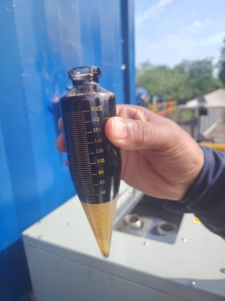 Tubo de centrífuga con muestra de crudo junto a la cabina de laboratorio